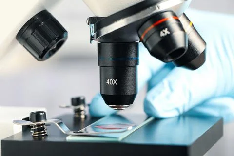 Scientist examining sample of red liquid on slide under microscope in laborat Stock Photos