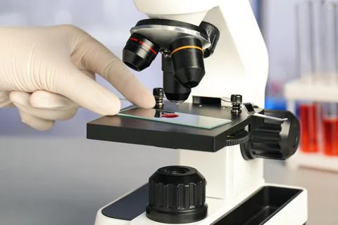 Scientist examining sample of red liquid on slide under microscope in laborat Stock Photos