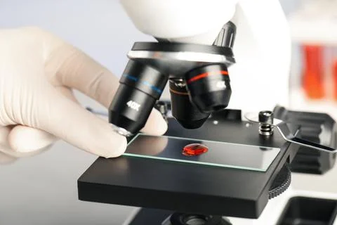 Scientist examining sample of red liquid on slide under microscope in laborat Stock Photos