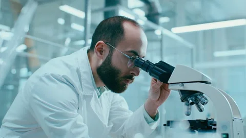Scientist Examining Sample through Microscope and Taking Notes in Laboratory Stockbeeldmateriaal 331336870