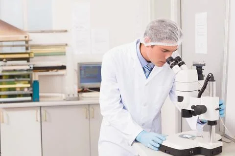 Scientist is examining samples using microscope on white lab bench with Stockfoto's