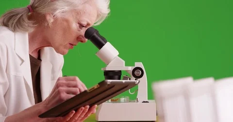 Scientist examining substance through microscope on greenscreen Video stock 79414036