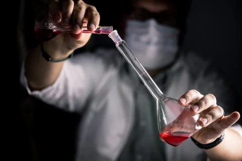 Scientist with face mask working with red liquid in a conical erlenmeyer flask Stock Photos