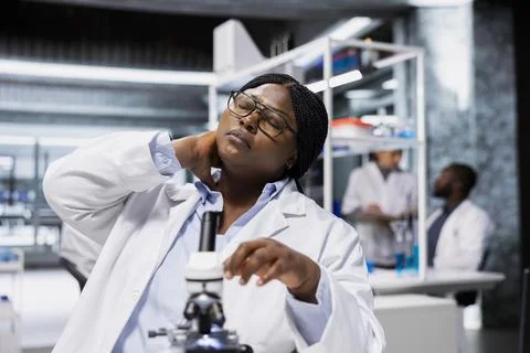 Scientist feeling neck pain while examining tissue under microscope Stock Photos
