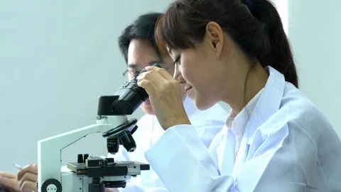 Scientist female is looking through microscope with colleagues working in lab. Video stock 108724794
