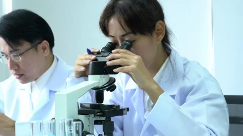 Scientist female is looking through microscope with colleagues working in lab. Video stock 108733110