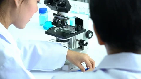 Scientist female is looking through microscope with colleagues working in lab. Video stock 108778552
