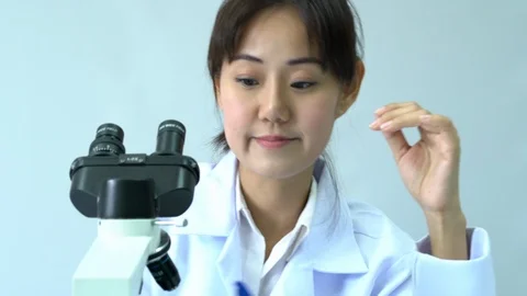 Scientist female is looking through microscope with colleagues working in lab. Video stock 108780476