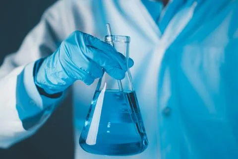 Scientist hand hold erlenmeyer flask with stirring rod filled with blue sam.. Stock Photos