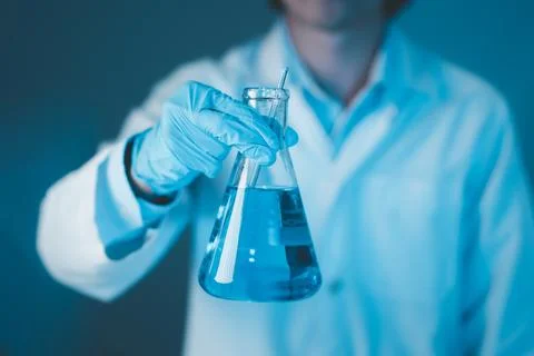 Scientist hand hold erlenmeyer flask with stirring rod filled with blue sam.. Stock Photos