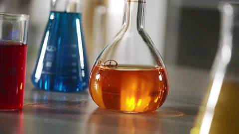Scientist hand places orange colored solution flask on table close up laboratory Video stock 312330754