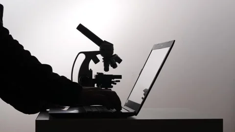 Scientist hands typing on a laptop next to a microscope, representing digital Stock Footage 347323614