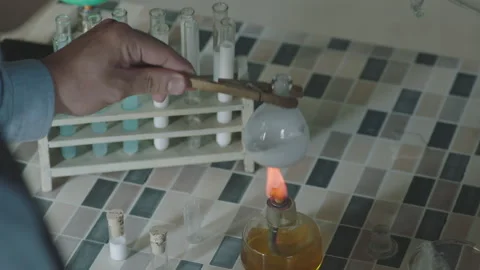 Scientist heating a round-bottom flask with a Bunsen burner in a laboratory Stock Footage 336233599