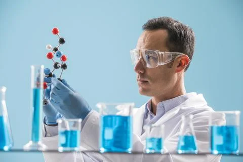 Scientist holding molecule model, blue liquid in beakers in foreground Stock Photos