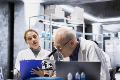 Scientist inspects drug under microscope helped by assistant reporting findings Stock Photos