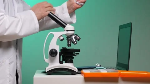 Scientist in lab coat cleaning a microscope objective lens by hand, prepping Stock Footage 347239328