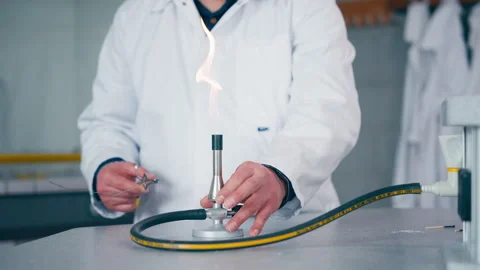 Scientist in lab coat lighting fire with burner in laboratory experiment Stock Footage 302823395