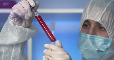 Scientist in the lab in a protective suit examines the blood tube. Closeup Video stock 129695776