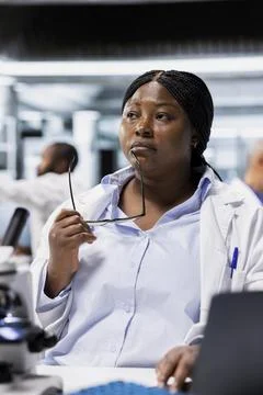 Scientist in lab thinking, analyzing clinical trial outcomes on laptop Stockfoto's