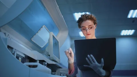 Scientist in laboratory analyzes data on laptop while interacting with advanced Stock Footage 334884700
