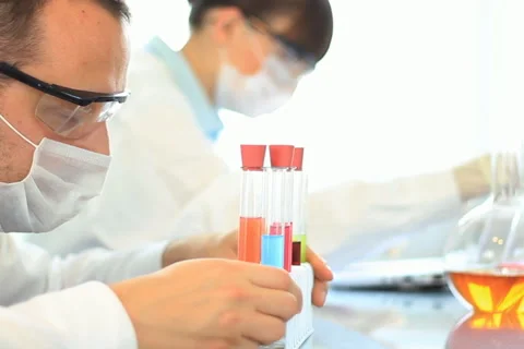 Scientist looking at test tubes with colorful liquid, female coworker in bg Stock Footage 5090334