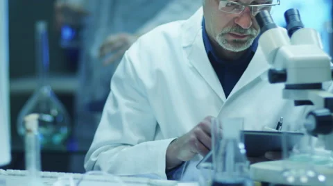 Scientist is Looking through Microscope and Writing Data on Tablet Stock-Footage 48417002