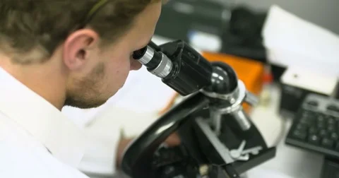 Scientist is Looking through Microscope and Writing Data on Tablet Video stock 70396100