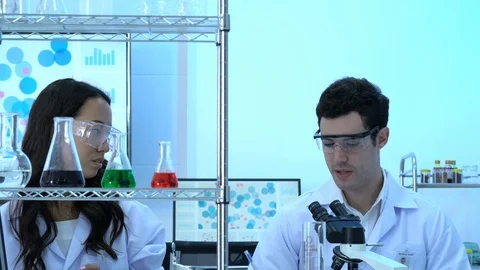 Scientist is looking through microscope with colleagues working in modern lab. Stock Footage 106867370