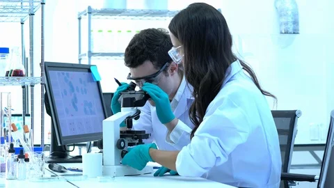Scientist is looking through microscope with colleagues working in modern lab. Stock Footage 106869364