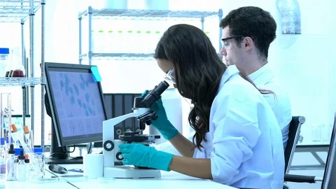 Scientist is looking through microscope with colleagues working in modern lab. Stock Footage 106869503