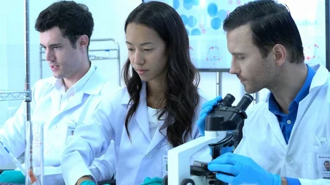 Scientist is looking through microscope with colleagues working in modern lab. Stock Footage 106870061