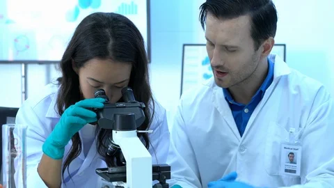 Scientist is looking through microscope with colleagues working in modern lab. Stock Footage 109135913