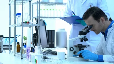 Scientist is looking through microscope with colleagues working in modern lab. Stock Footage 109138540