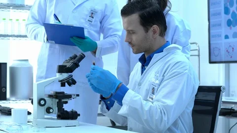 Scientist is looking through microscope with colleagues working in modern lab. Stock Footage 109138662