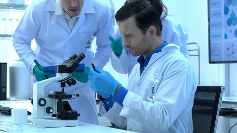 Scientist is looking through microscope with colleagues working in modern lab. Stock Footage 109139145