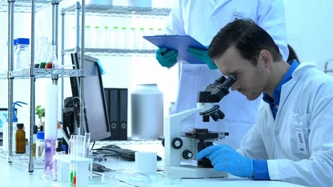 Scientist is looking through microscope with colleagues working in modern lab. Stock Footage 109139742