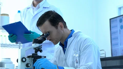 Scientist is looking through microscope with colleagues working in modern lab. Stock Footage 111659670