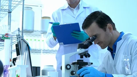 Scientist is looking through microscope with colleagues working in modern lab. Stock Footage 111663254