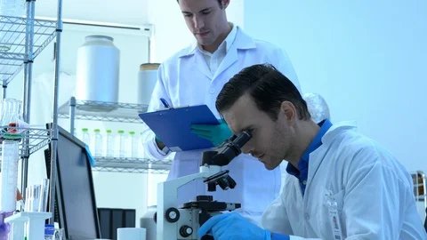 Scientist is looking through microscope with colleagues working in modern lab. Stock Footage 111665970