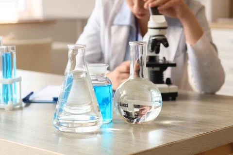 Scientist looking through microscope with laboratory glassware Stock Photos