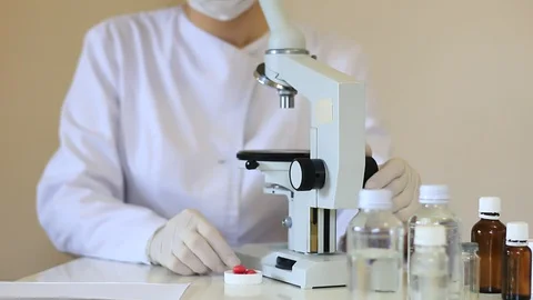 Scientist Looks at Biological Samples Under Microscope and Reports about Virus Stock Footage 127865359