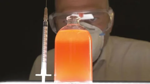 Scientist looks at orange bubbling liquid in a bottle and syringe Stock Footage 156334771