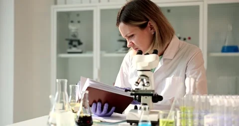 Scientist looks through a microscope and leafs through book Stock Footage 251735029
