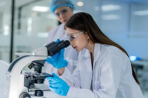 Scientist looks through microscope in laboratory while another researcher o.. Stock Photos