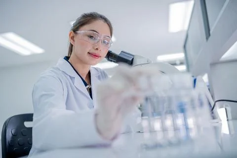 Scientist looks through microscope while holding up test tubes in laborator.. Stock Photos