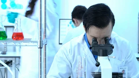 Scientist male is looking through microscope with colleagues working in lab. Stock Footage 106870672