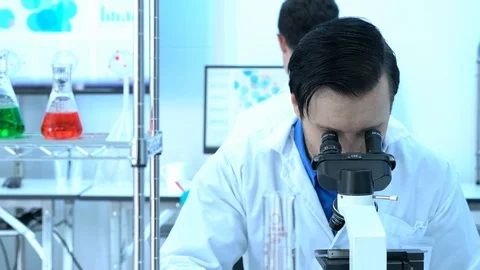 Scientist male is looking through microscope with colleagues working in lab. Video stock 106870799