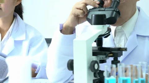 Scientist male is looking through microscope with colleagues working in lab. Video stock 108720699
