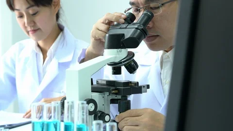 Scientist male is looking through microscope with colleagues working in lab. Stock Footage 108722469