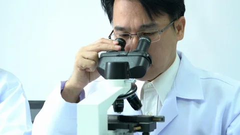 Scientist male is looking through microscope with colleagues working in lab. Video stock 108724363